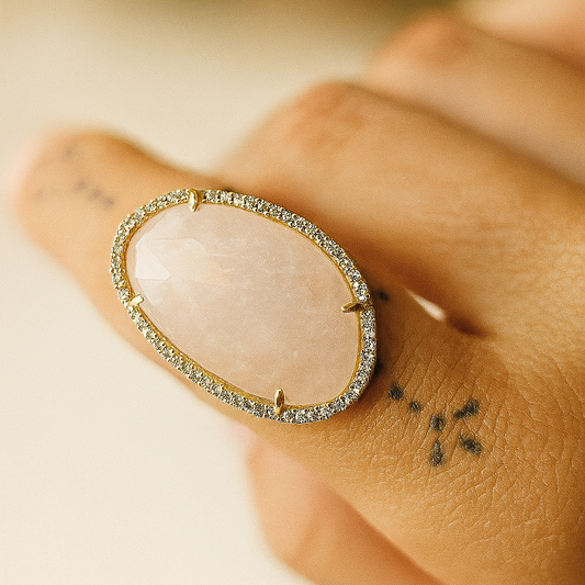 Anillo de cuarzo rosa para mujer estilo bohemio con engaste dorado y detalles brillantes, fotografía de joyería artesanal sobre fondo neutro.